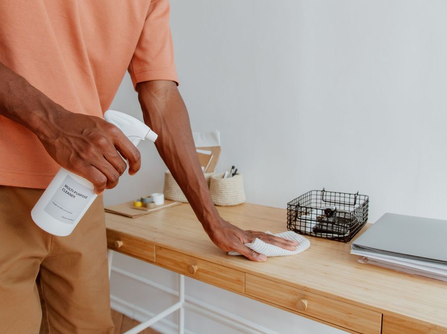 A cleaner wiping down a desk with a spray bottle and cloth